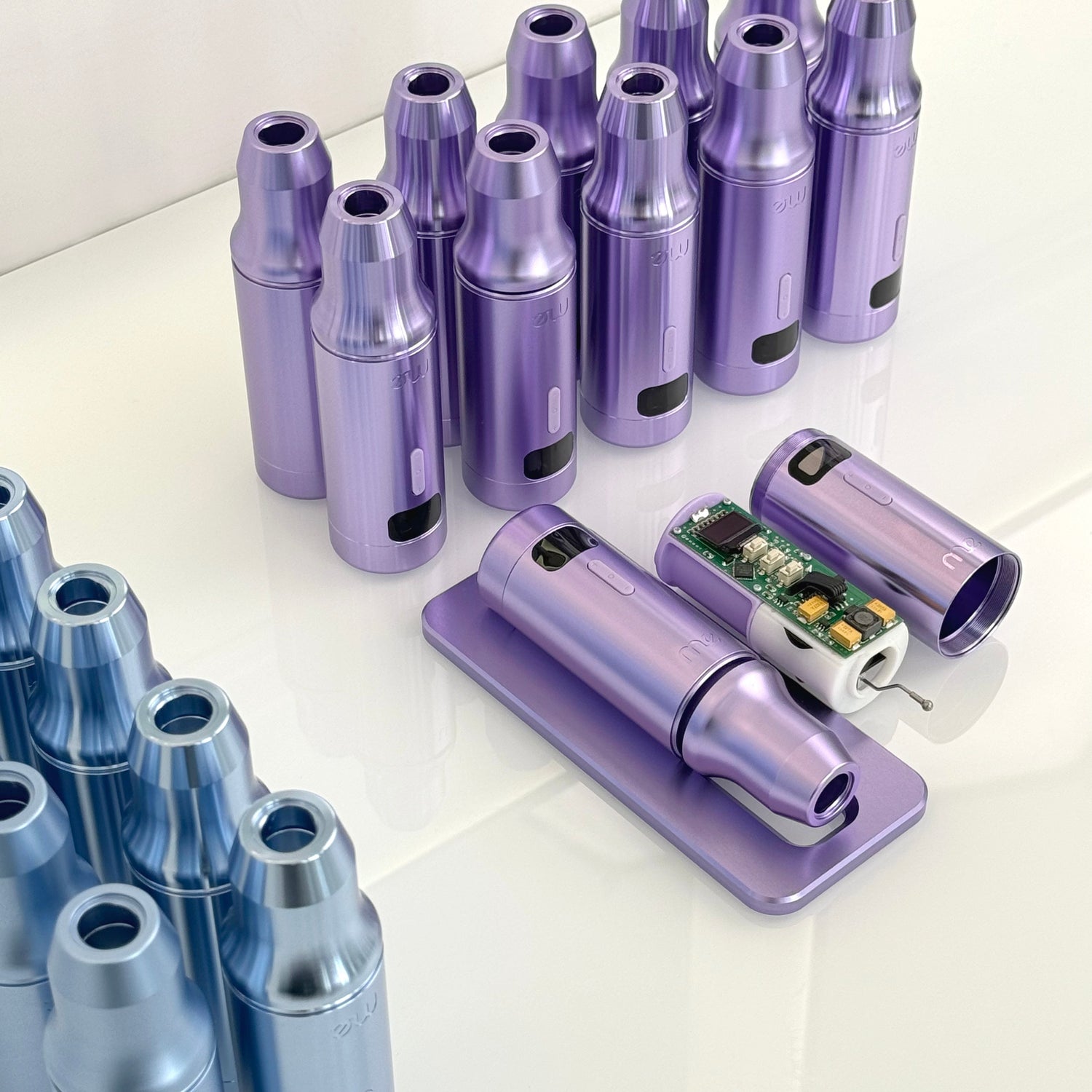 Violette und blaue Gehäuse von Permanent Make-up Maschinen auf weißer Oberfläche, das Innere eines Geräts zeigt die Elektronik.